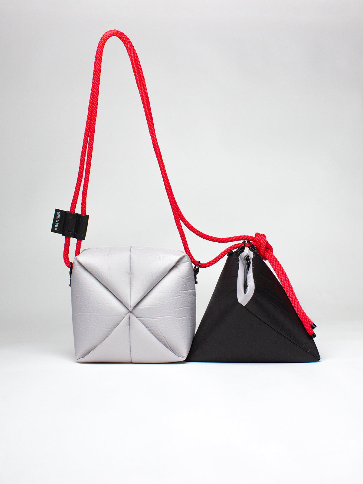 Two geometrically shaped bags, one white and one black, with a red strap on a light gray background.